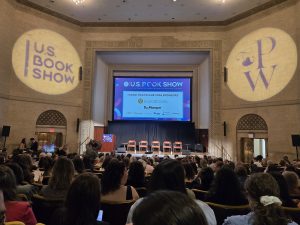 auditorium facing a stage set with 5 chairs, a podium and a screen featuring the US Book Show 2026 sponsor logos