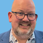 image of a bearded bald man, wearing eyeglasses, a blue blazer, and a patterned shirt